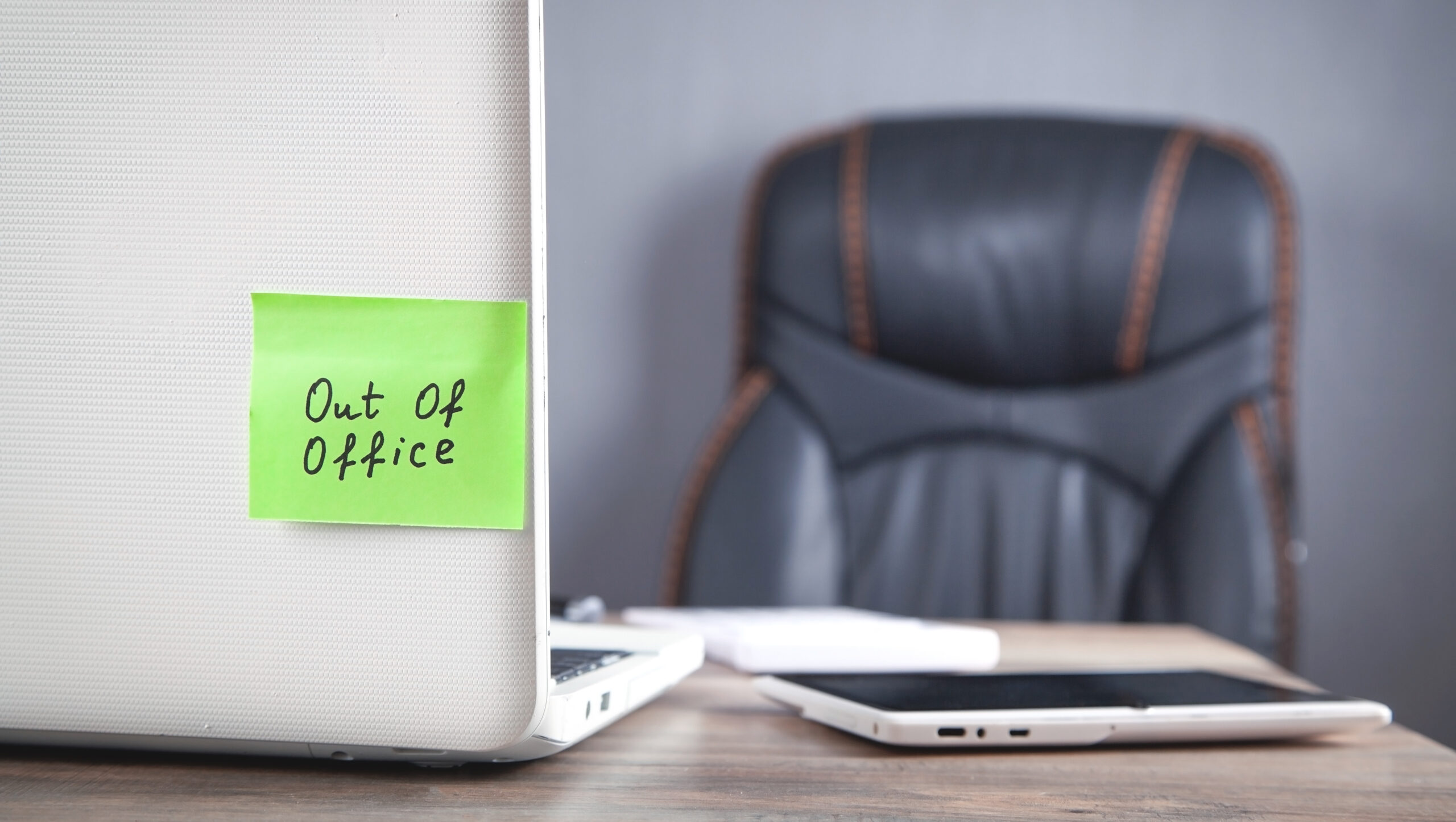 Out of office message on sticky note with computer.